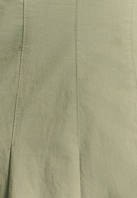 Vihreä kangas, jossa on teksturoitu pinta, pystysaumoja ja hienovaraisia poimutusdetaljeja. Pehmeä ja kevyt materiaali.