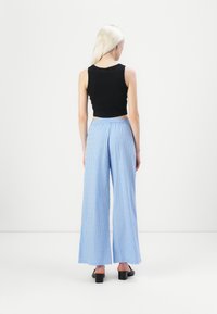 Zwarte mouwloze crop top en blauw gestreepte wijde broek met kleine decoratieve stippen. Glad materiaal met een elastische taille. Zwarte blokhak schoenen.
