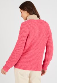 Maglione rosa fluffy con una texture a coste e un colletto alto beige, con maniche lunghe e una vestibilità rilassata, mostrato di spalle.