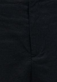 Gros plan sur un tissu noir avec une couture verticale et une texture subtile, suggérant un vêtement ou un rembourrage.