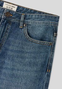 Jeans in denim blu scuro con un classico design a cinque tasche, caratterizzati da cuciture dorate e una chiusura con bottone in vita. Etichetta visibile.