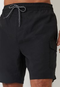 Czarne kąpielówki wykonane z lekkiego materiału, z elastycznym pasem ze sznurkiem, boczną kieszenią typu cargo oraz gładką strukturą.