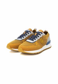 Zapatos deportivos amarillos y grises con parte superior de malla, acentos de ante, cordones azules, un talón texturizado y una suela blanca en contraste.