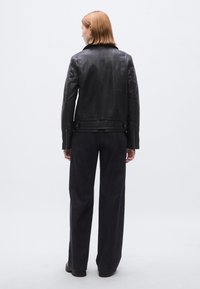 Schwarze Lederjacke mit figurbetontem Design, stehendem Kragen und Reißverschlussbündchen, kombiniert mit weiten dunkelblauen Jeanshosen.