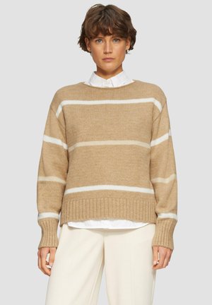 Pull en tricot beige avec des rayures blanches, manches et ourlet côtelés. Porté par-dessus une chemise blanche à col. Texture douce et coupe décontractée.