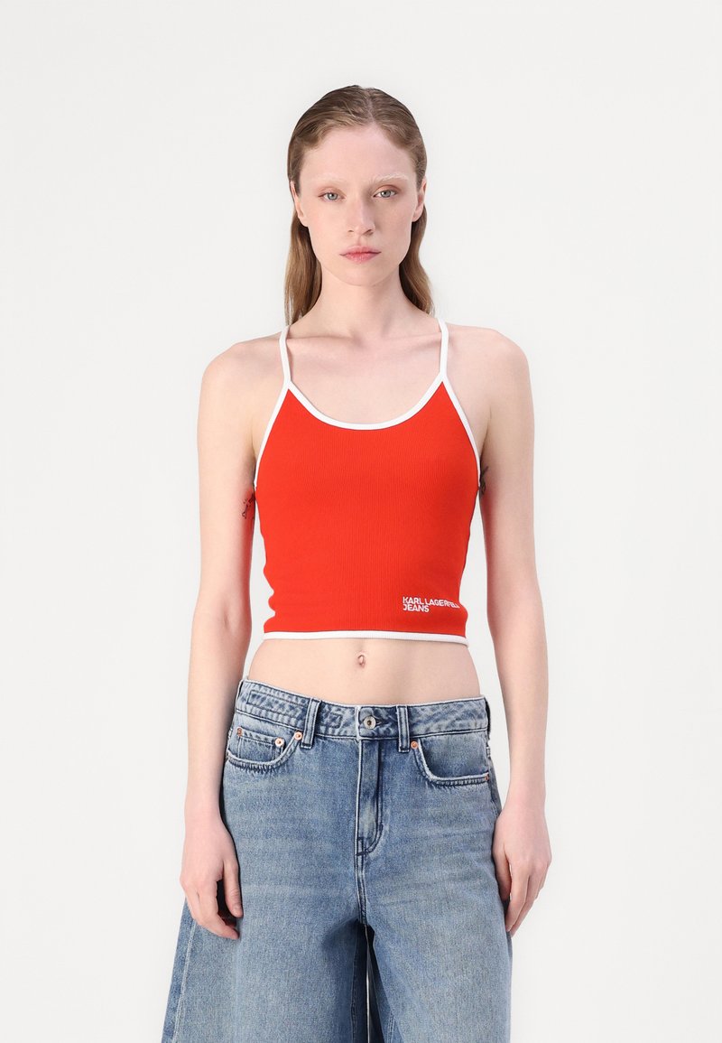 Top court côtelé rouge avec des bretelles fines et un bord blanc, comportant un logo en texte blanc. Assorti à un jean en denim bleu clair taille haute.