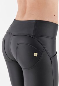 Leggings negros de tiro alto fabricados con una tela suave y elástica. Presentan costuras curvas y un pequeño parche de logo en el bolsillo trasero.