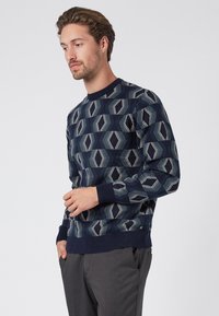 Navy blue sweater with geometric pattern in shades of blue and cream. Ribbed round neckline and cuffs, lightweight knit texture.