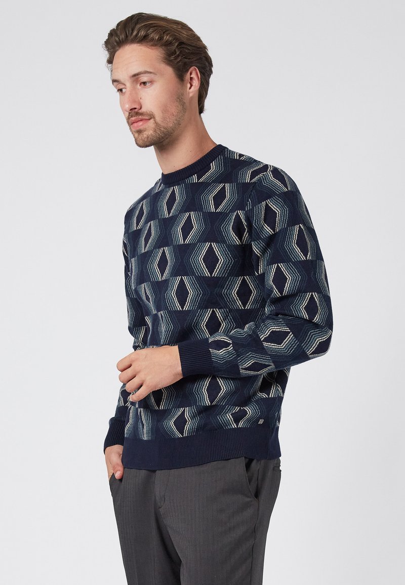 Navy blue sweater with geometric pattern in shades of blue and cream. Ribbed round neckline and cuffs, lightweight knit texture.