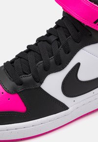 Vysoké tenisky s čiernym koženým zvrškom, bielymi a jasne ružovými akcentmi, textúrovanými šnúrkami a polstrovanou ružovou podrážkou.