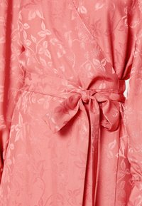 Rosa tyginpackningsklänning med subtila blommönster, en knytbeltsaxel och långa ärmar. Texturen verkar slät och lätt.