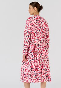 Langemouwige wikkeljurk met een roze achtergrond en navy en rode bladerenpatronen, gemaakt van zachte stof met een strikdetail rond de taille.