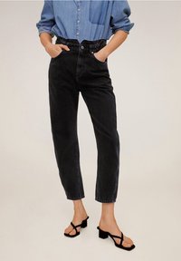 Jean en denim noir taille haute avec une coupe décontractée et des ourlets retroussés, associé à des sandales noires à brides et une chemise bleu clair à boutons.