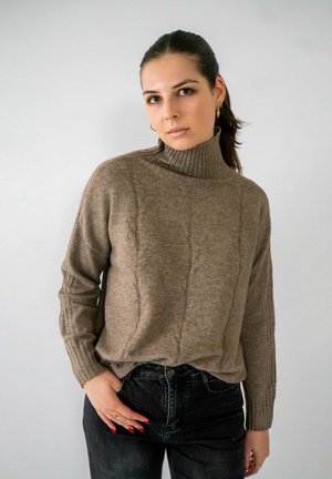 Pull en maille beige à col roulé avec des poignets côtelés, associé à un jean noir taille haute. Texture lisse et coupe décontractée.