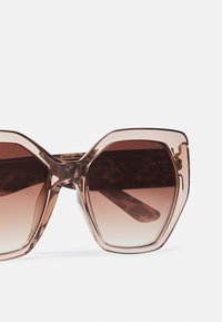 Ochelari de soare mari, hexagonali, cu rame transparente de culoare maro deschis și lentile graduare de culoare maronie, având un model țestoasă pe brațe.
