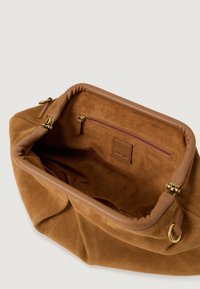 Interno della borsa in suede marrone con rifiniture in pelle liscia. Presenta una tasca con zip e un'etichetta con logo impresso. Design morbido e strutturato.