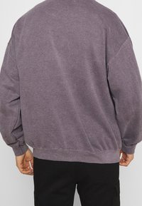 Felpa viola in cotone con vestibilità morbida, spalle scese e polsini a coste. Il tessuto ha una superficie morbida e leggermente strutturata.