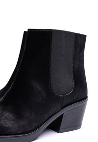 Stivaletti neri alla caviglia con una texture liscia simile alla pelliccia, pannelli laterali elastici e un tacco a blocco robusto. Design minimalista con linee pulite.