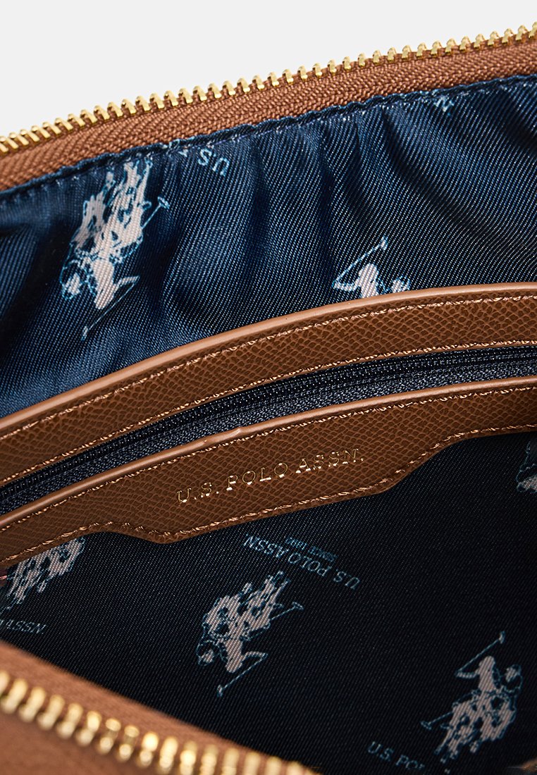 Interior de una bolsa de cuero marrón texturizado con un forro azul oscuro que presenta un patrón repetido del logo de U.S. Polo Assn. y un zipper dorado.