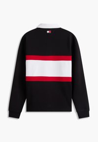Sweat-shirt noir à manches longues avec col blanc, large bande horizontale blanche bordée de rouge sur le dos, et petit logo Tommy Hilfiger sous le col.