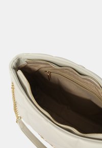 Borsa a tracolla bianca trapuntata con una superficie liscia, hardware dorato e dettagli in catena. L'interno presenta una tasca con zip e una foderatura beige.