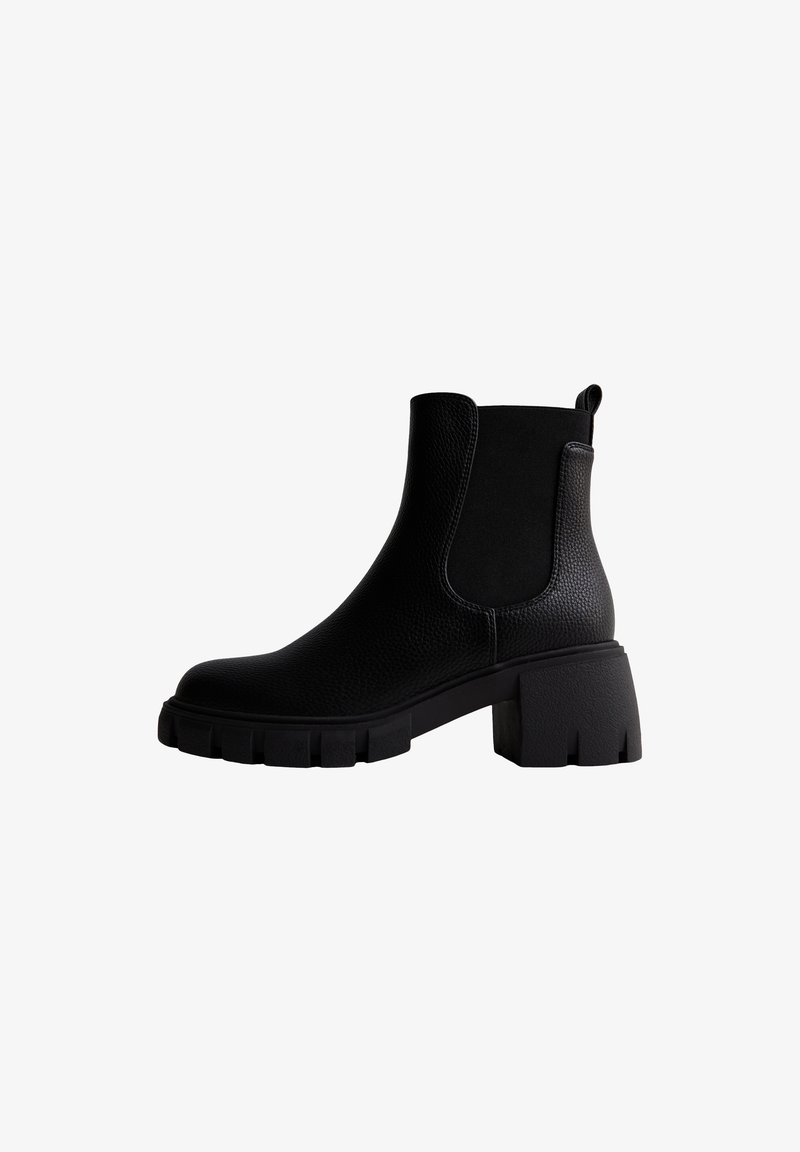 Bottine noire en cuir avec semelle crantée épaisse, talon cubain, panneaux latéraux élastiques et languette à l'arrière.