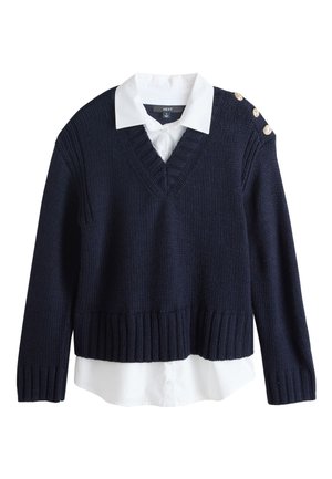 Granatowy sweter z dzianiny z dekoltem w serek, ściągaczem na dole i mankietach, trzema dekoracyjnymi złotymi guzikami na ramieniu, noszony na białą koszulę z kołnierzykiem.