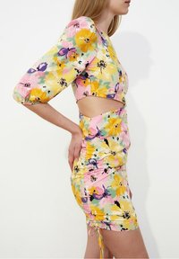 Blommig miniklänning med en färgpalett i gult, rosa och lila, puffärmar, sidoutskärning, rynkad textur och justerbar knytning i nederkant.