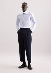 Lichtblauw button-up shirt met een geruit patroon, gecombineerd met donkerblauwe plooibroeken en zwarte nette schoenen.