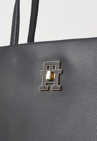 Black textured leather handbag featuring a prominent gold and black logo detail. Two sturdy handles are visible at the top.