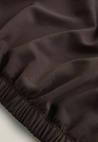 Dunkelbrauner Stoff mit glatter Textur und einem elastischen Saum, der das Material zusammenzieht. Die Oberfläche weist einen dezenten Glanz auf.