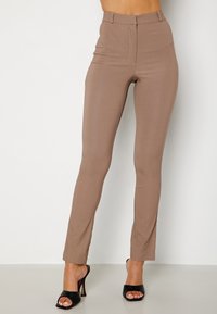 Pantalon marron taille haute en tissu extensible, coupe ajustée avec des coutures verticales, assorti à des talons noirs ouverts à l\'avant.