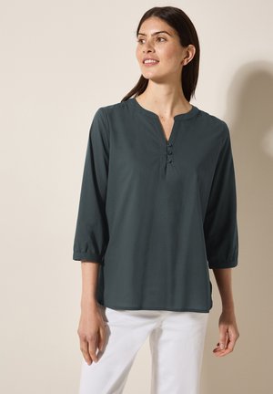Blusa verde scuro a maniche lunghe con colletto alla cinese e tre bottoni al collo; tessuto morbido con una superficie liscia e vestibilità comoda.