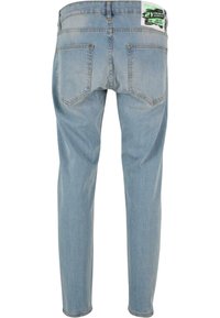 Vaaleansiniset farkut, joissa on slim fit -leikkaus, kahdella takataskulla ja vihreällä tarralla vyötärönauhasta. Havaittavissa on kulutettua pintaa.