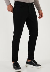 Svart denimbyxor med smal passform, med en slät yta, fem fickor och blå stygn som detaljer. Matchas med svarta sneakers.