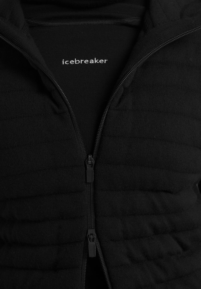 Schwarze gesteppte Jacke mit doppeltem Reißverschluss, teilweise geöffnet, zeigt die schwarze Innenschicht mit dem weißen "icebreaker"-Logo auf der Brust.