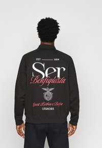 Black sweatshirt with embroidered graphics on the back. Features white and pink text, a central emblem, and a ribbed neckline and cuffs.