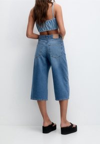 Culottes de mezclilla azul con un corte relajado, que presentan una cintura de media altura y dos bolsillos traseros. Combinados con sandalias de plataforma negras.