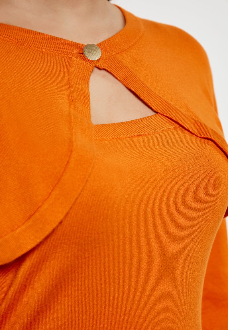 Top lavorato a maglia arancione con scollo rotondo, caratterizzato da un design a chiave fissato da un bottone dorato. Tessuto liscio e forma aderente.