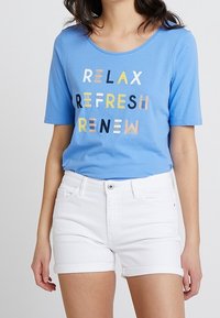 Vaaleansininen lyhythihainen t-paita pyöreällä pääntiellä, jossa teksti "RELAX REFRESH RENEW" monivärisin kirjaimin. Yhdistetty valkoisiin shortseihin.