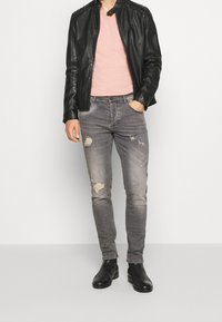 Black leather jacket over a pink T-shirt, paired with gray distressed jeans and black ankle boots. Simple, fitted design with minimal detailing.