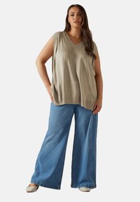 Beige ärmlös topp med V-ringning, tillsammans med ljusblå vida jeans och neutrala slip-on skor. Slät textur och avslappnad passform.