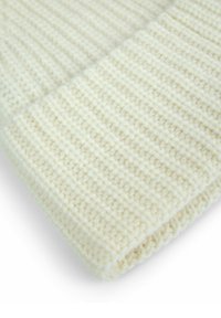 Primo piano di un tessuto lavorato a maglia di colore crema piegato, con una texture a coste e punti visibili.