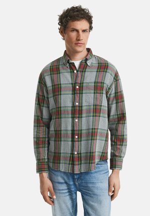 Chemise à manches longues à carreaux dans un motif vert, rouge et blanc. Présente un col boutonné et des boutons blancs. Associée à un jean bleu clair.