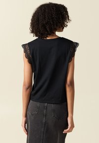 Svart bomullstopp med korta ärmar och scallop-lace detaljer. Bakifrån syns en figurnära design och en slät yta.