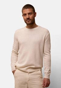Helle beigefarbene Wollpullover mit Rundhalsausschnitt und gerippten Bündchen. Die Textur ist weich und der Schnitt ist lässig. Dezente Details am Saum.