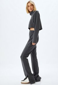 Grijze cropped sweatshirt met een hoge hals en lange mouwen, gecombineerd met bijpassende fitted broek met een gespleten zoom en een elastische tailleband.