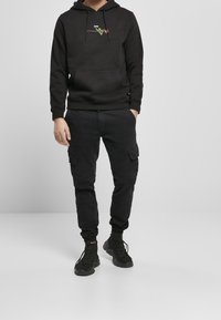 Felpa nera con cappuccio, con ricami di una rosa e la scritta "love", abbinata a pantaloni cargo neri e sneakers nere, con una vestibilità comoda.