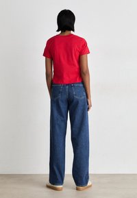 Röd kortärmad croppad t-shirt i kombination med löst sittande blå jeans, med hög midja, bakfickor och en enkel design.