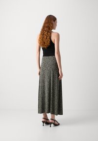 Falda maxi con un estampado animal negro y beige, de diseño fluido, combinada con una parte superior ajustada negra y tacones negros con tiras.